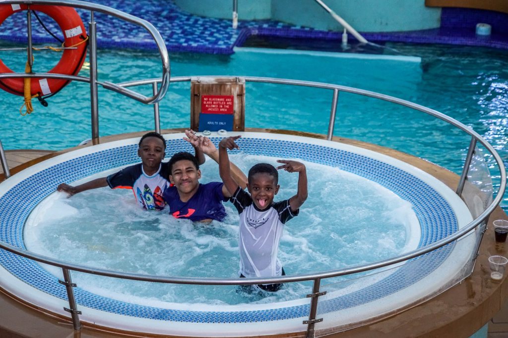 several boys celebrating in a hot tub by a swimming pool